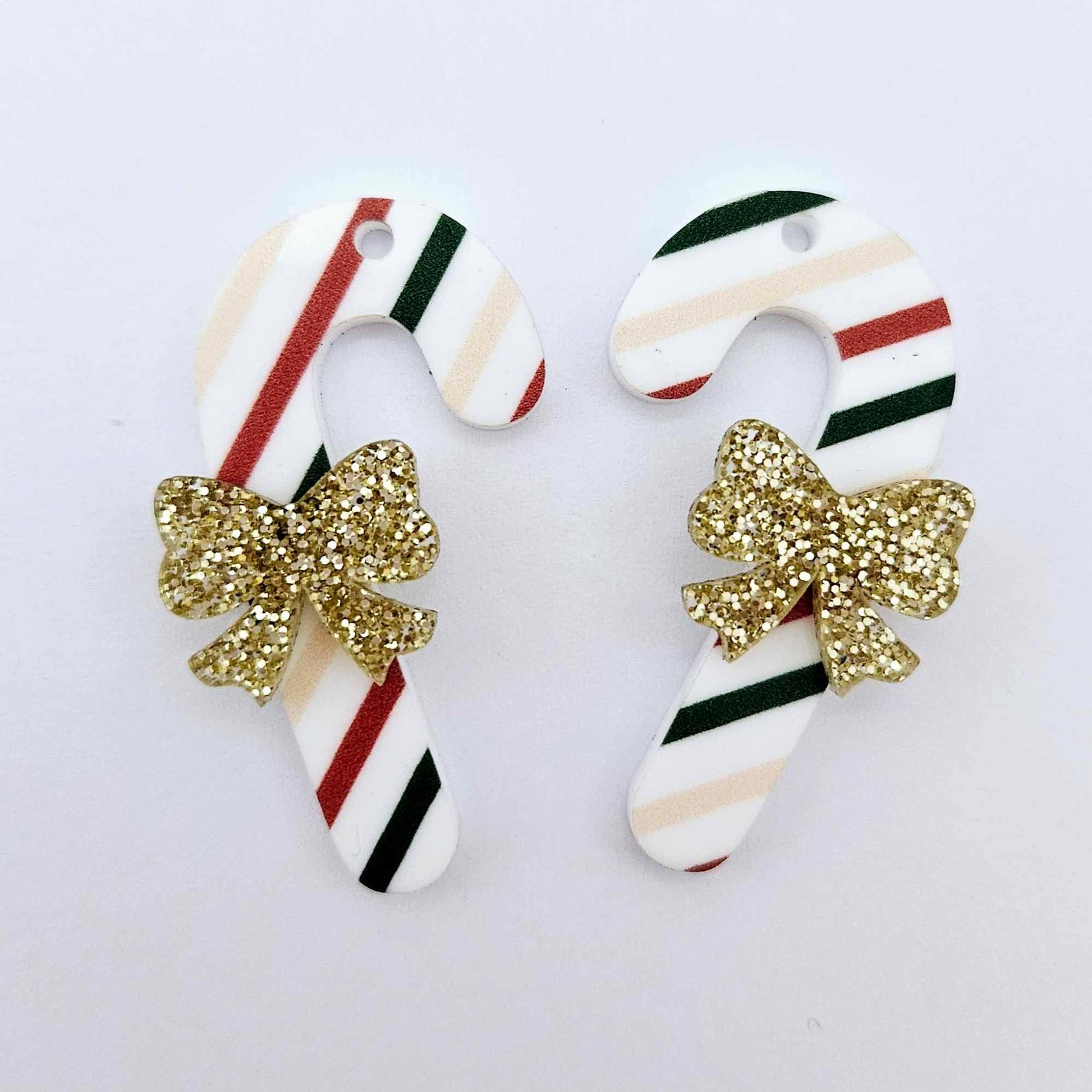 One pair of Stripy Christmas UV printed acrylic candy cane dangle earring blanks laying flat with gold glitter bows attached