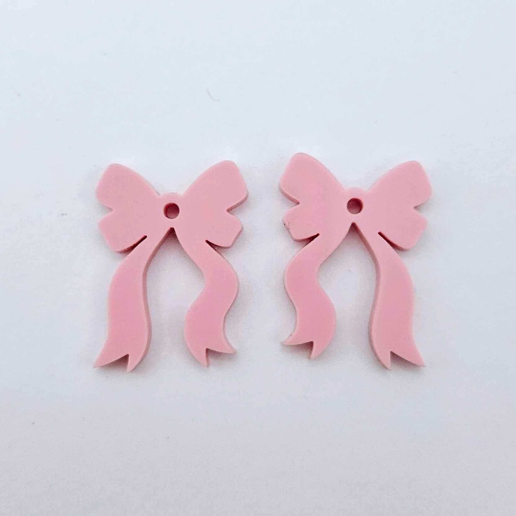 One pair of pastel pink acrylic bow dangle earring blanks laying flat
