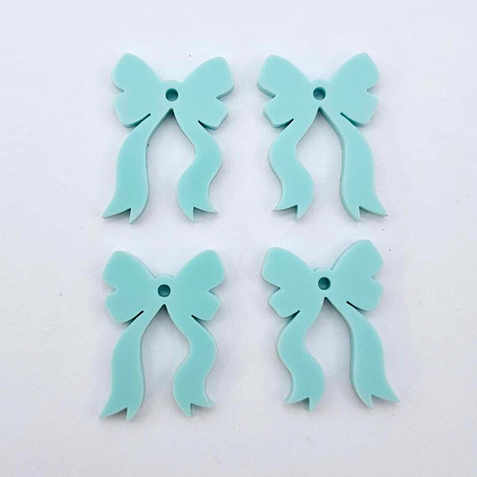 Two pairs of pastel aqua acrylic bow dangle earring blanks laying flat