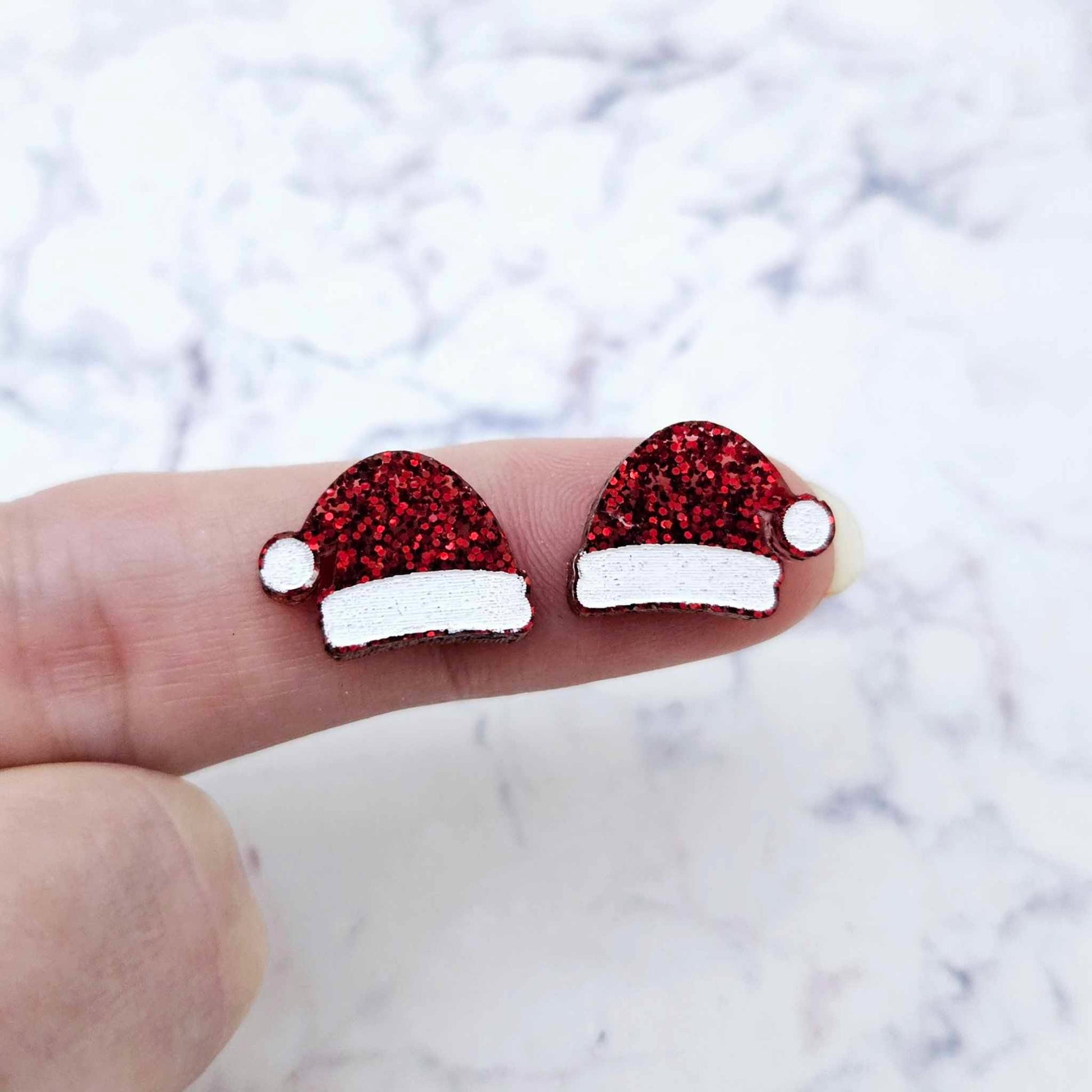 One pair of paint-filled red glitter Santa hat stud blanks (no hole) shown on a finger for size reference