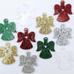 A mixture of gold glitter, red glitter, green glitter, silver glitter and Fairy Dust Glitter acrylic 32mm angel dangle earring blanks laying flat on a white background