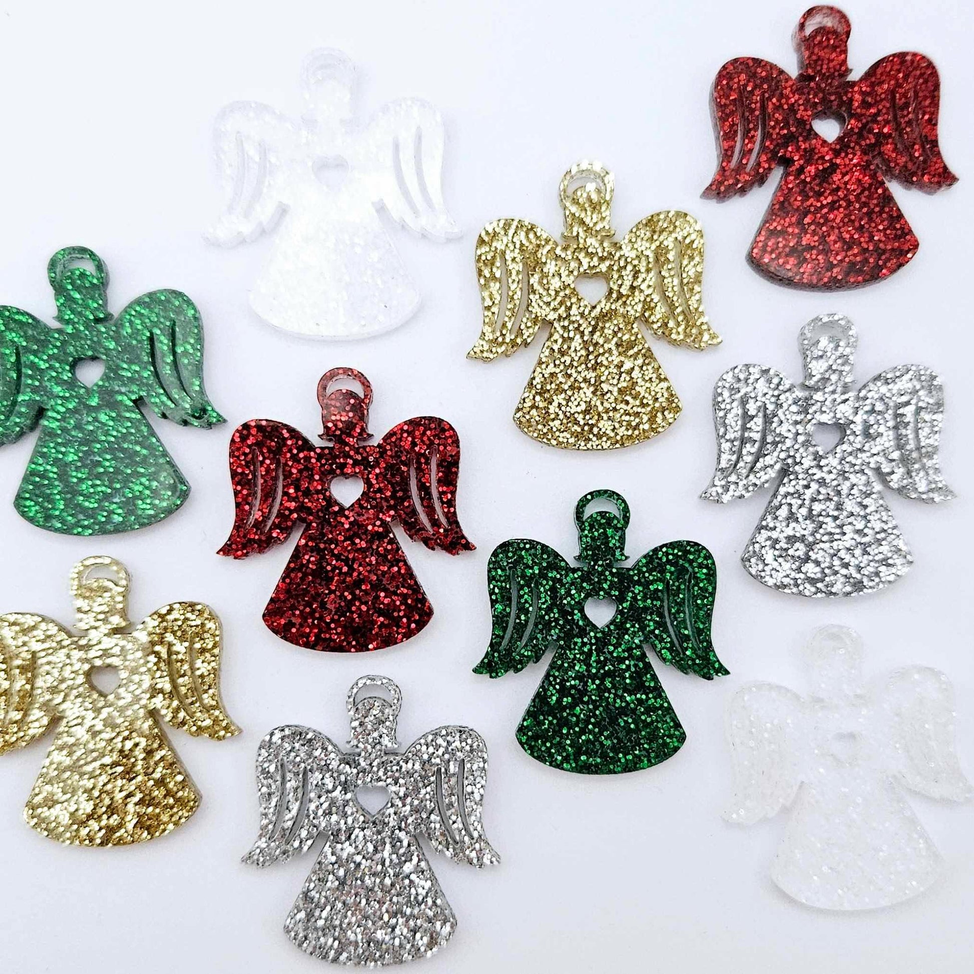 A mixture of gold glitter, red glitter, green glitter, silver glitter and Fairy Dust Glitter acrylic 32mm angel dangle earring blanks laying flat on a white background