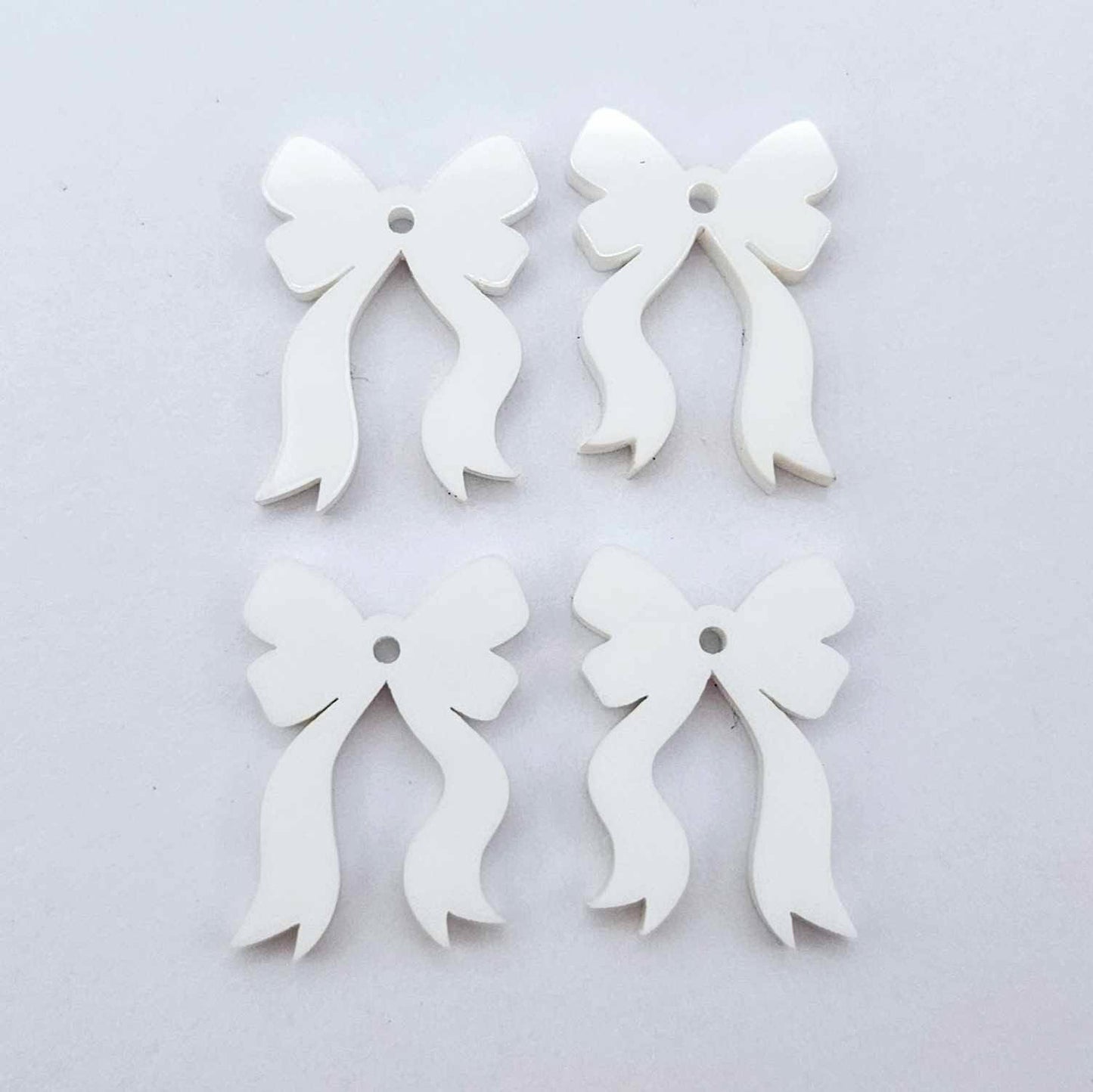 Two pairs of white acrylic bow dangle  earring blanks laying flat