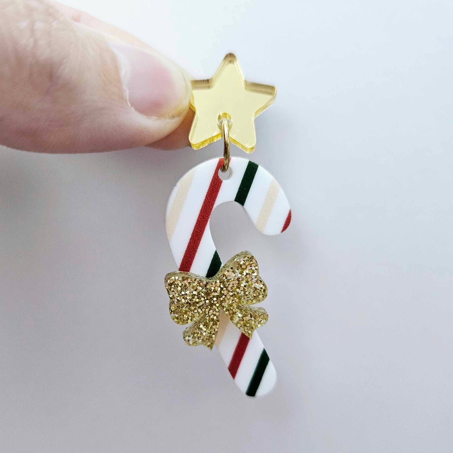 One Stripy Christmas UV printed acrylic candy cane dangle earring blank assembled with a gold glitter bow and a 16mm gold mirror star topper, shown as a finished festive earring