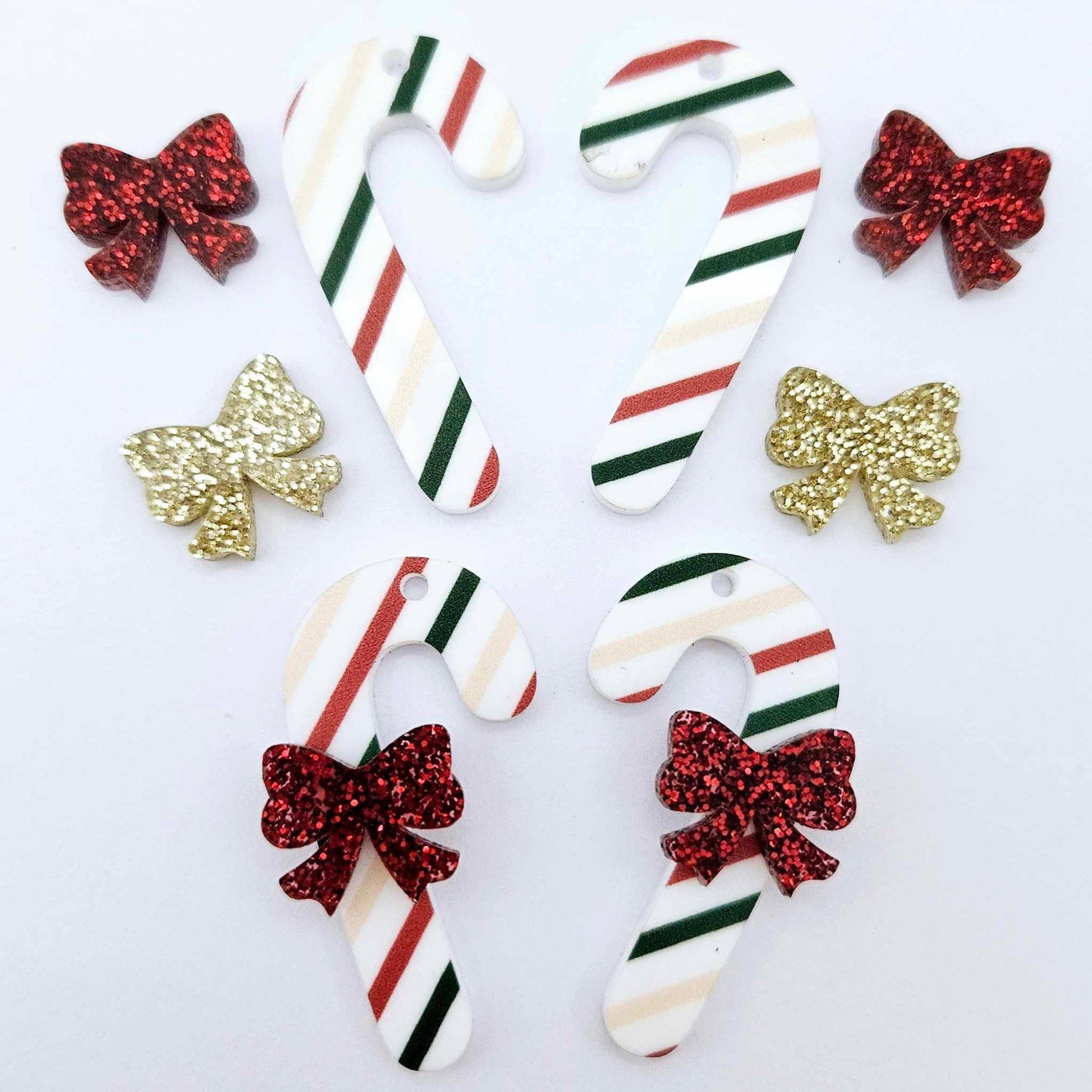 Two pairs of Stripy Christmas UV printed acrylic candy cane dangle earring blanks laying flat, decorated with red/gold glitter bows 