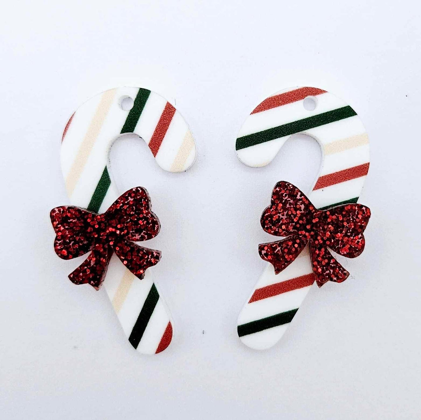 One pair of Stripy Christmas UV printed acrylic candy cane dangle earring blanks laying flat with red glitter bows attached