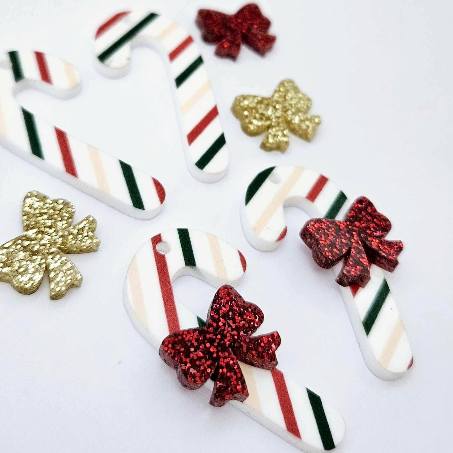 Two pairs of Stripy Christmas UV printed acrylic candy cane dangle earring blanks laying flat, decorated with red/gold glitter bows 