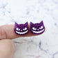One pair of 16mm holographic purple glitter acrylic Spooky Cat stud earring blanks with white paint-filled facial details shown on a finger for size reference