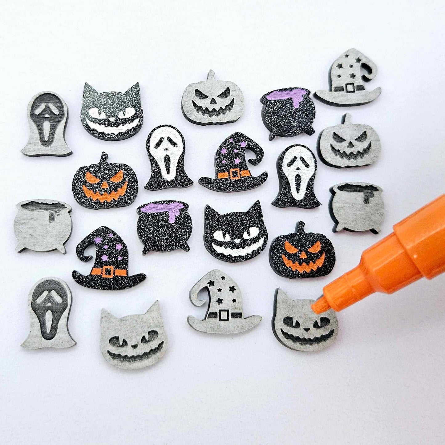 A mixed selection of black glitter Halloween stud earring blanks featuring Spooky Cats, Witch’s Cauldrons, Jack-O’-Lanterns, Spooky Face Masks and Witch’s Hats laying flat