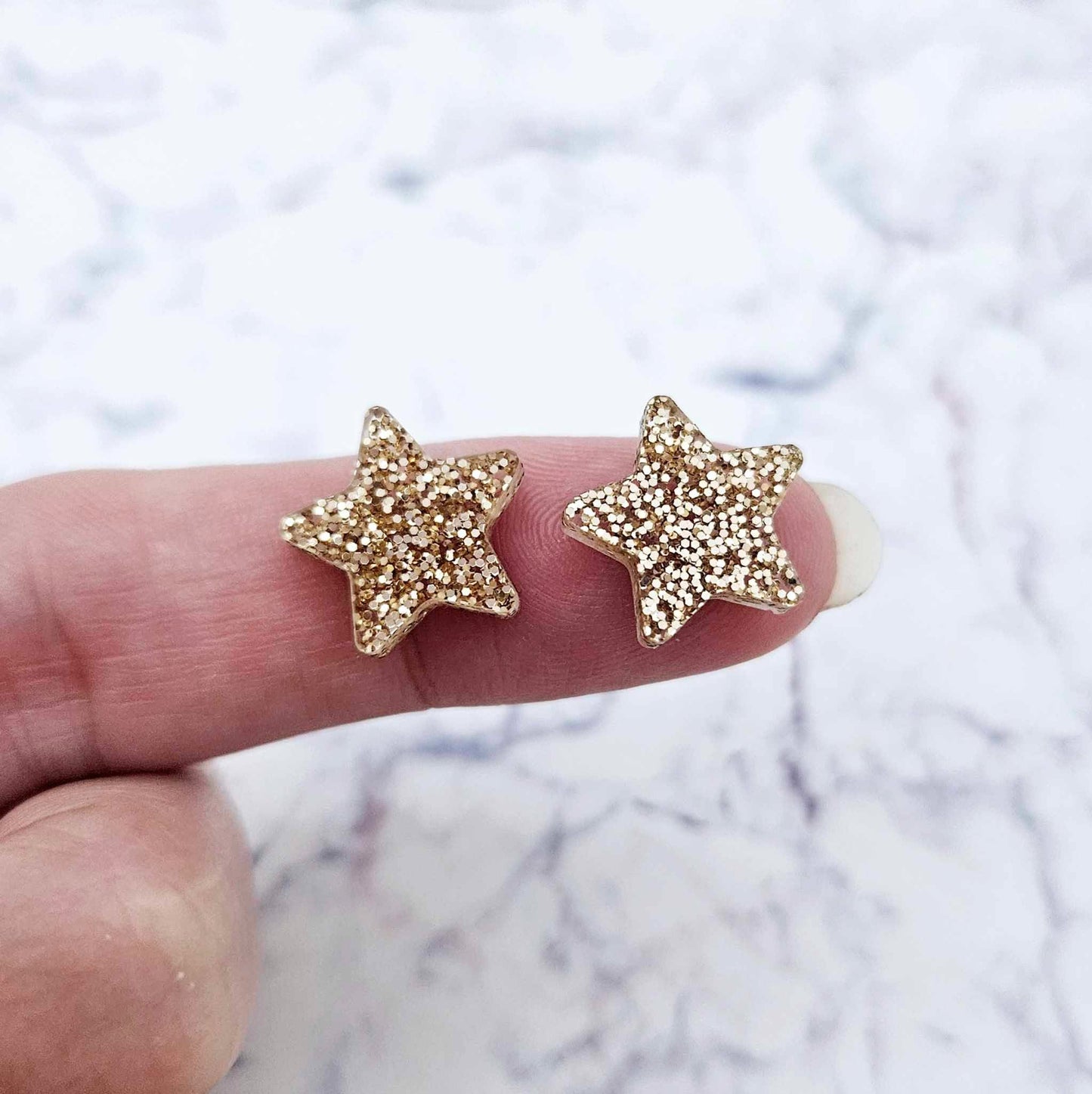 One pair of 14mm rose gold glitter acrylic star stud earring blanks shown on a finger for size reference