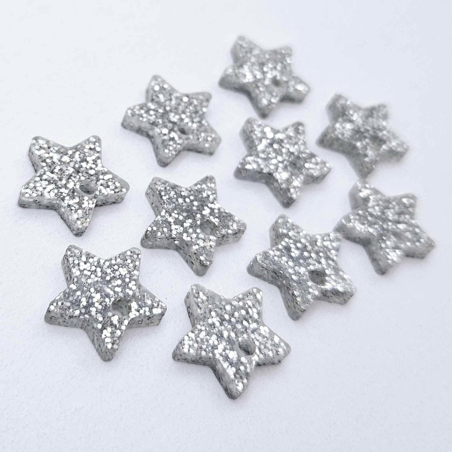 Five pairs of 14mm silver glitter acrylic star earring toppers laying flat
