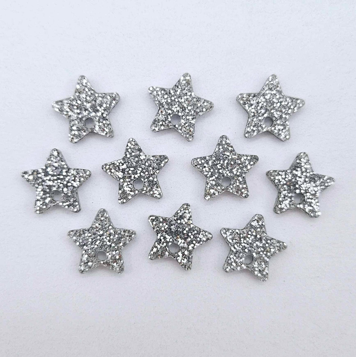 Five pairs of 14mm silver glitter acrylic star earring toppers laying flat