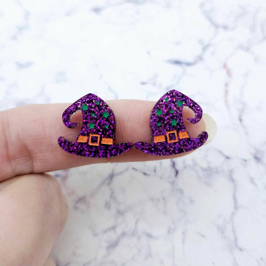 One pair of 18mm holographic purple glitter acrylic witch’s hat stud earring blanks with orange and green paint-filled details shown on a finger for size reference