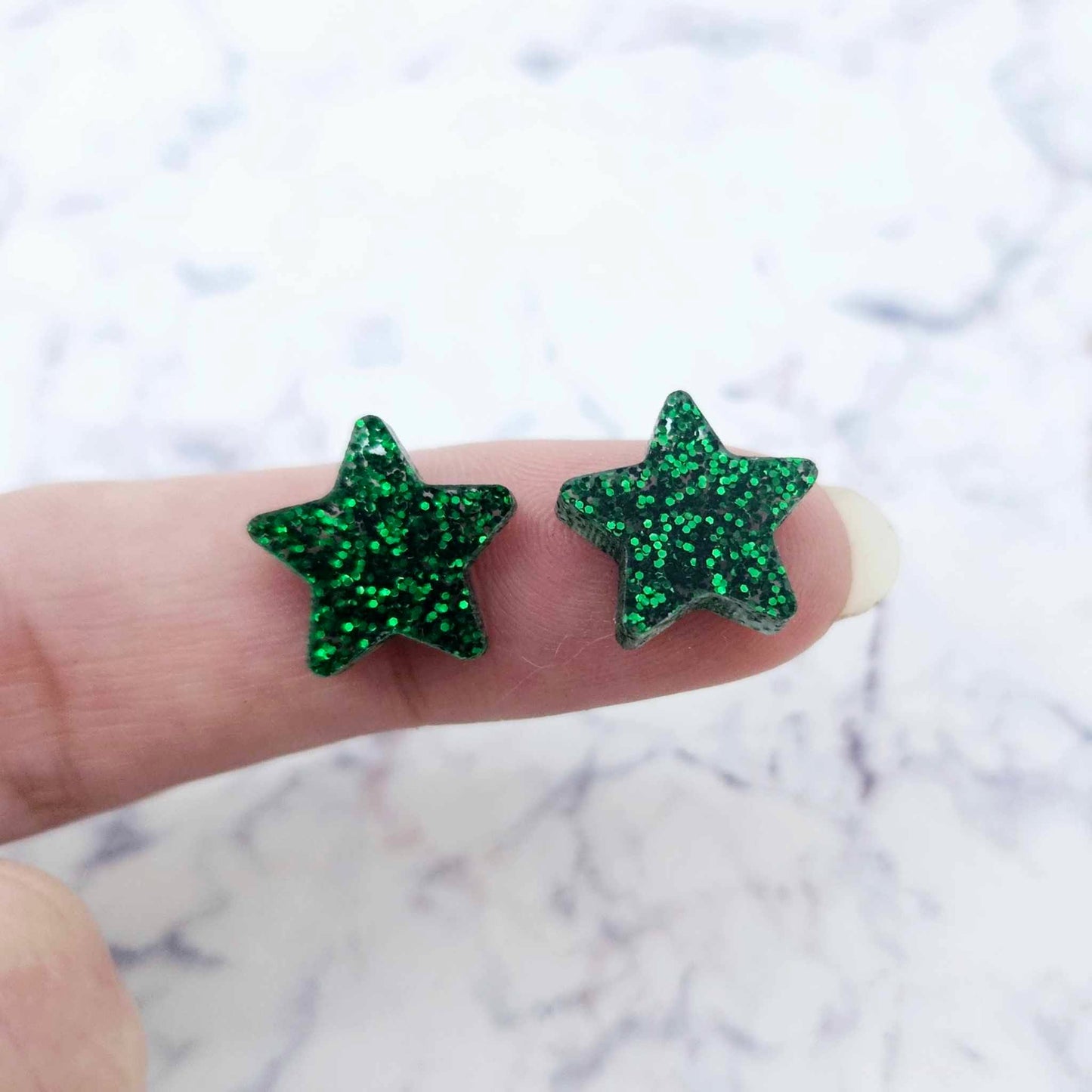One pair of 14mm green glitter acrylic star stud earring blanks shown on a finger for size reference