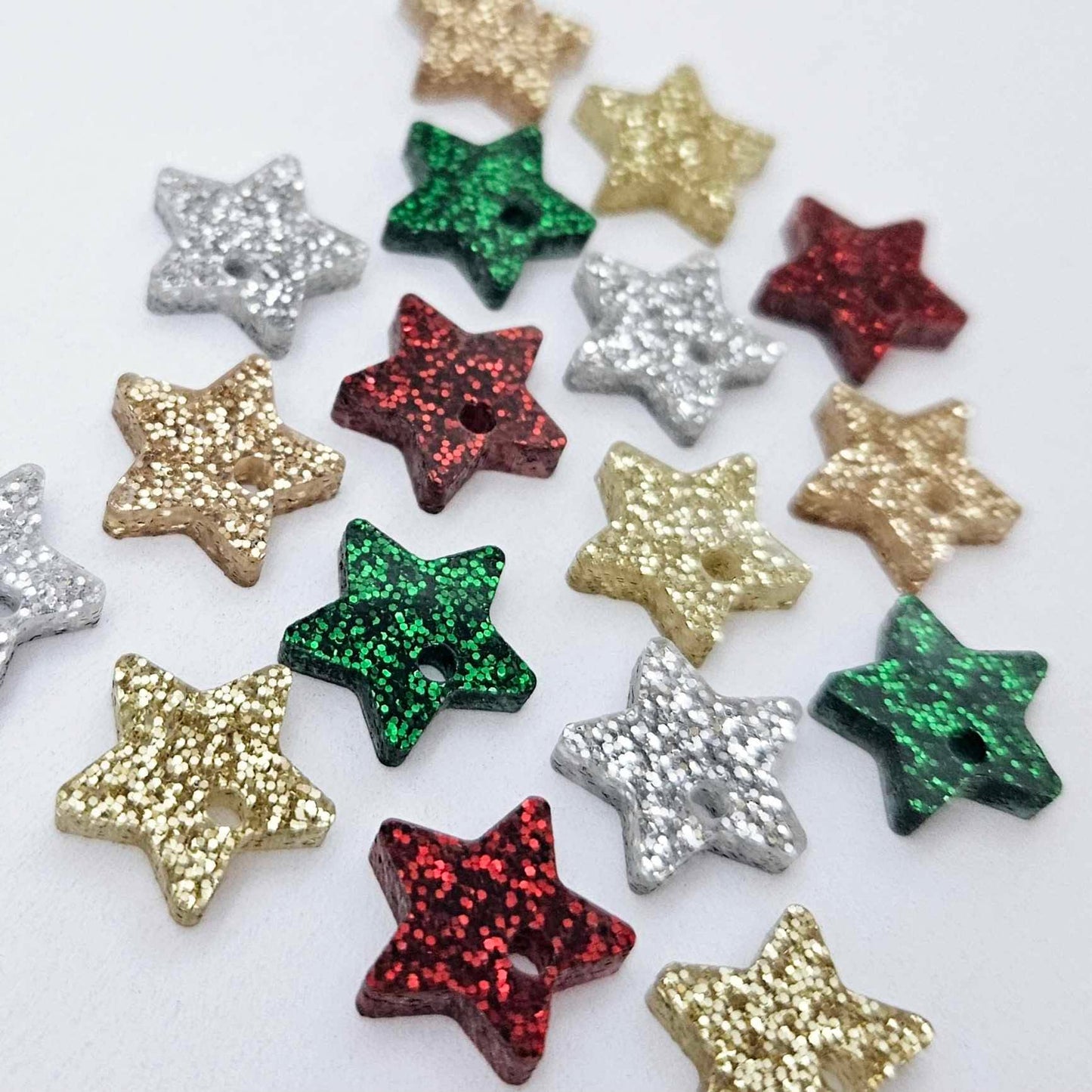 A selection of 14mm fine glitter acrylic star earring toppers in gold, silver, green, red and rose gold glitter laying flat