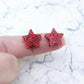 One pair of 14mm red glitter acrylic star stud earring blanks shown on a finger for size reference