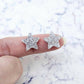 One pair of 14mm silver glitter acrylic star stud earring blanks shown on a finger for size reference