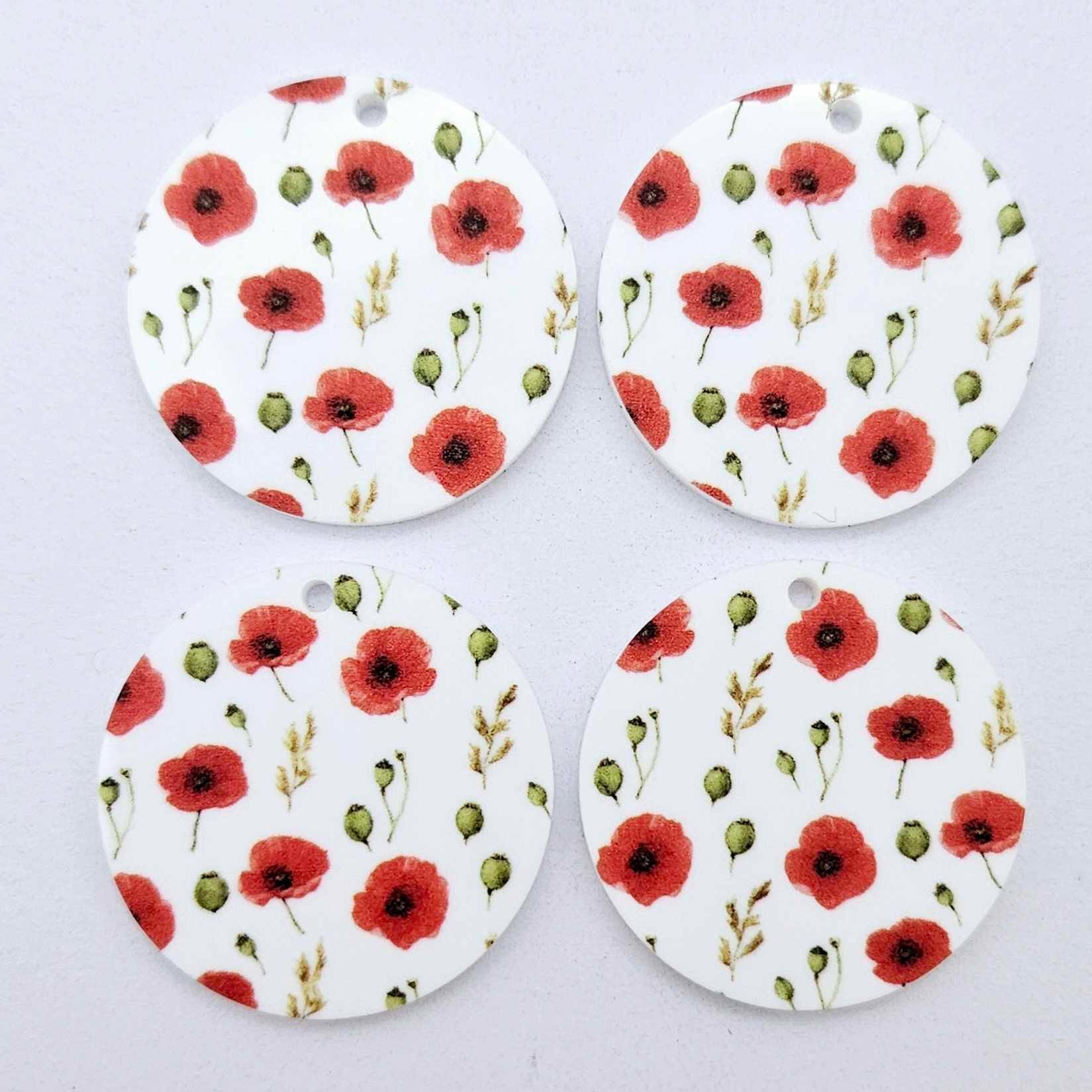 Two pairs of 32mm Poppy UV printed circle dangle earring blanks featuring detailed red poppies and green foliage on white acrylic laying flat.