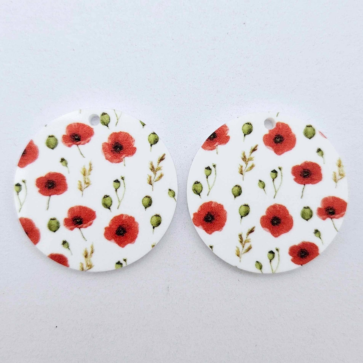 One pair of 32mm Poppy UV printed circle dangle earring blanks featuring vibrant poppy blooms and green foliage on white acrylic laying flat.