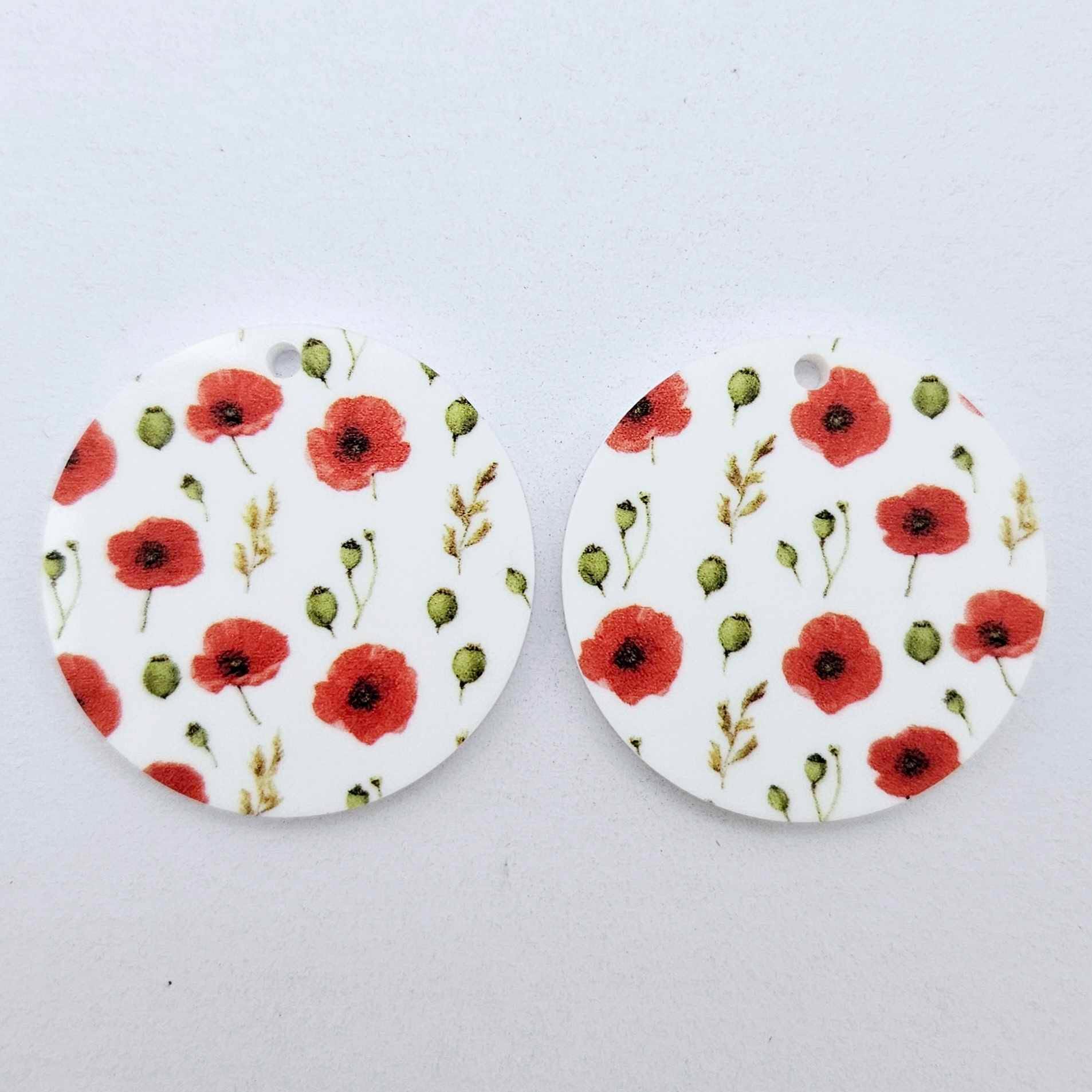 One pair of 32mm Poppy UV printed circle dangle earring blanks featuring vibrant poppy blooms and green foliage on white acrylic laying flat.