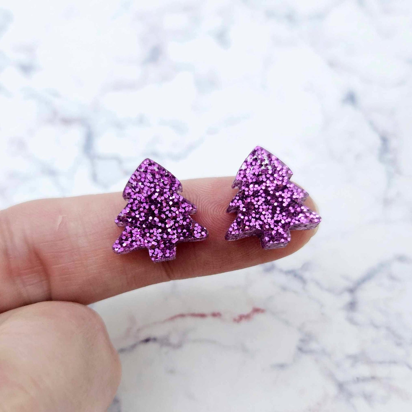 One pair of 16mm purple glitter Christmas tree stud earring blanks shown on a finger for size reference.