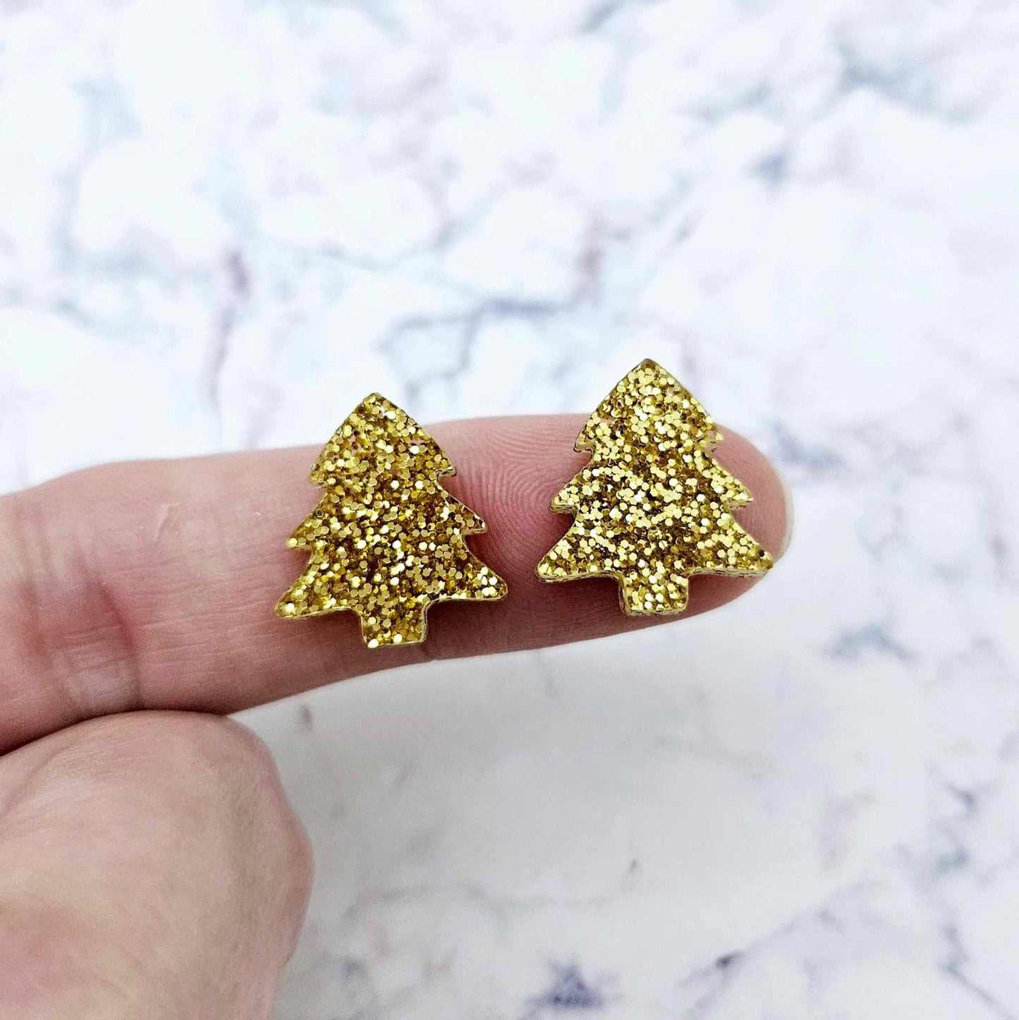 One pair of gold glitter acrylic 16mm Christmas tree stud blanks, shown on a finger for size reference.