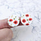 One pair of 20mm Poppy UV printed stud earring blanks featuring vibrant poppy blooms and green foliage on white acrylic, shown on a finger for size reference.