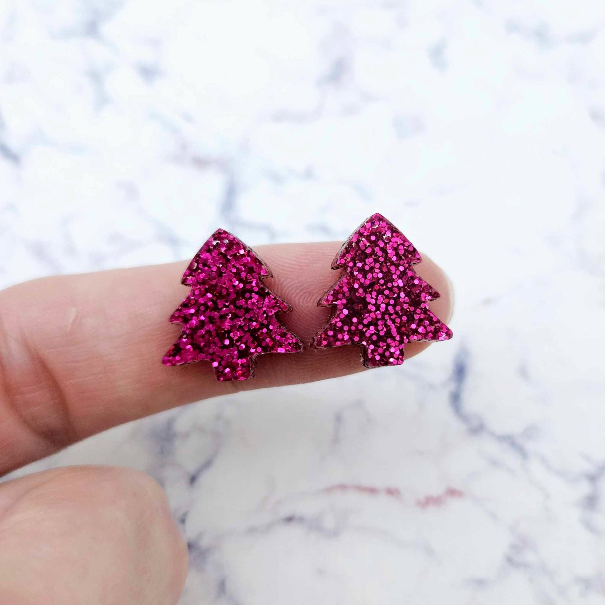 One pair of 16mm hot pink glitter Christmas tree stud earring blanks shown on a finger for size reference.