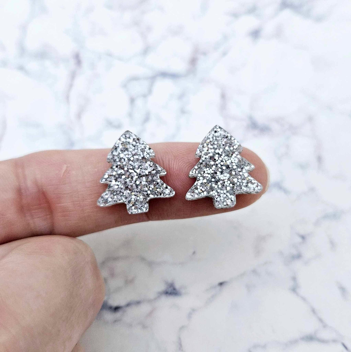 One pair of silver glitter acrylic 16mm Christmas tree stud blanks, shown on a finger for size reference.