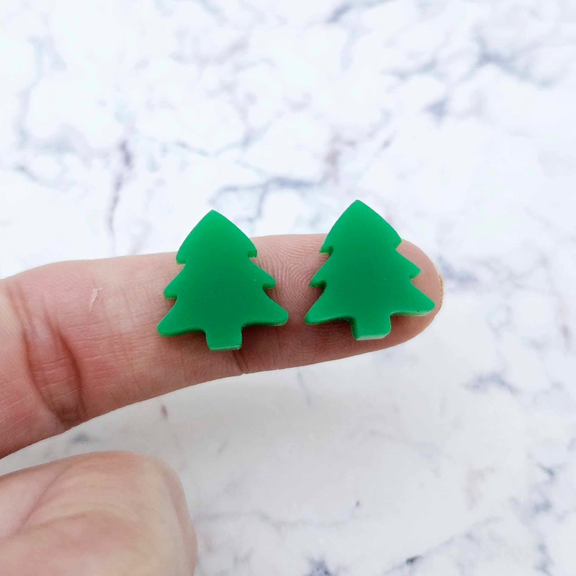 One pair of 16mm Solid Green acrylic Christmas tree stud earring blanks shown on a finger for size reference.