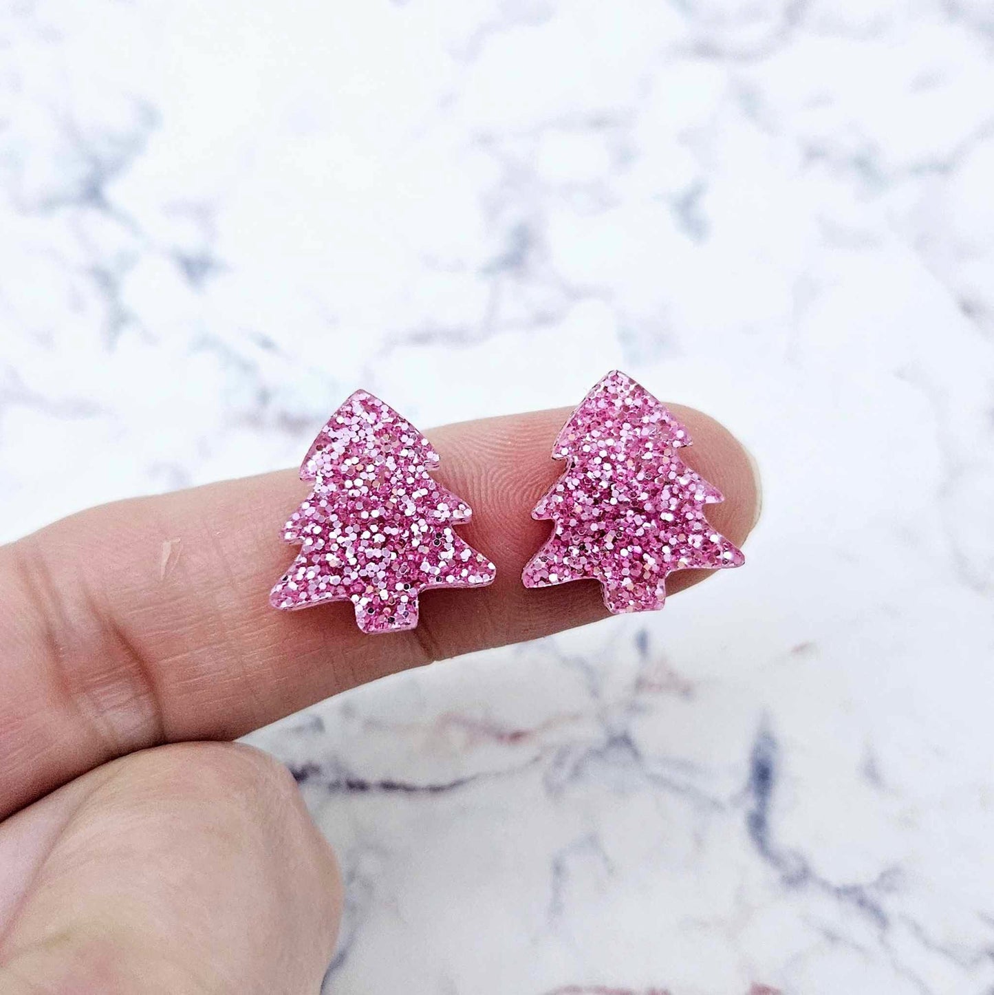 One pair of 16mm pink glitter Christmas tree stud earring blanks shown on a finger for size reference.