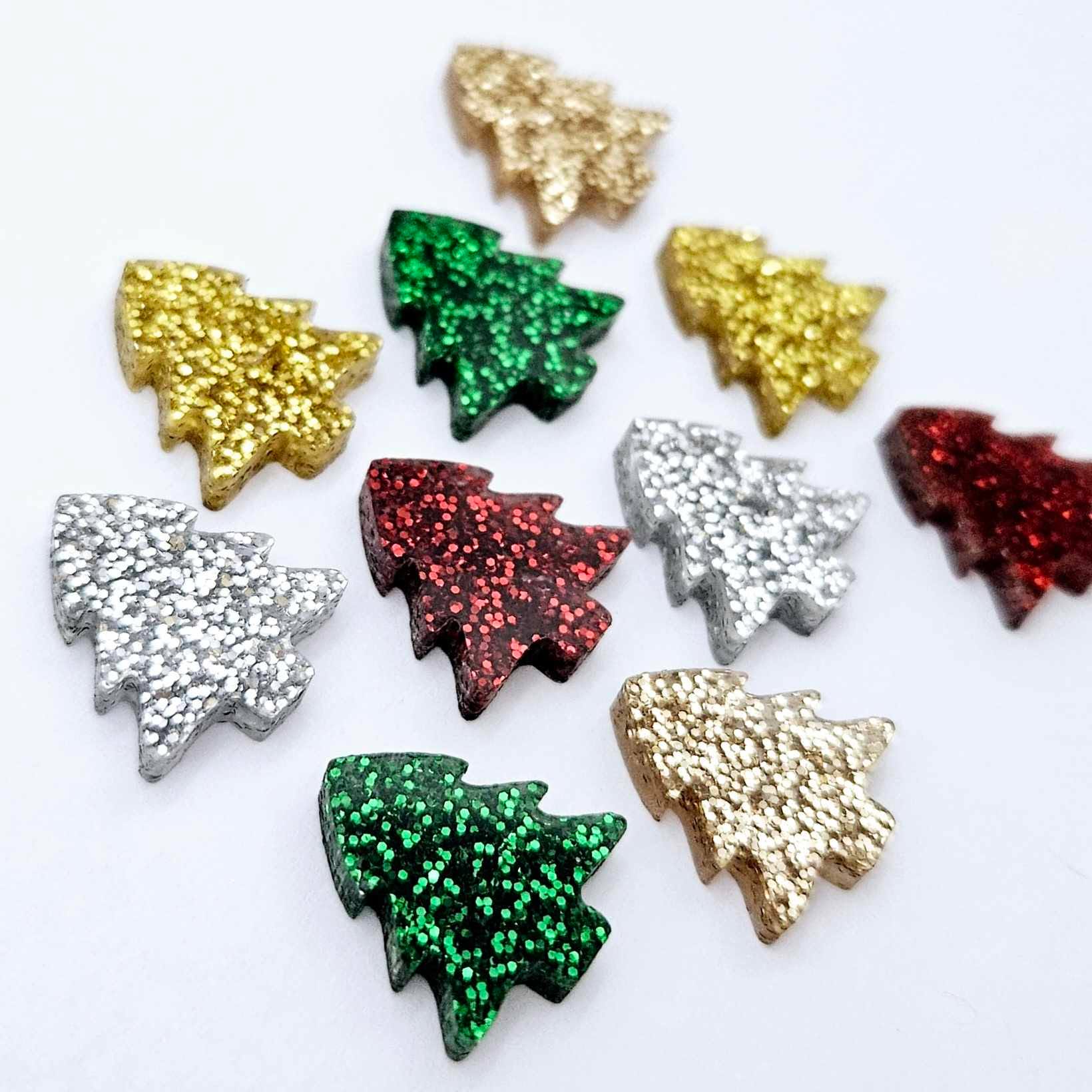 Traditional fine glitter acrylic 16mm Christmas tree stud earring blanks in festive colours laying flat.