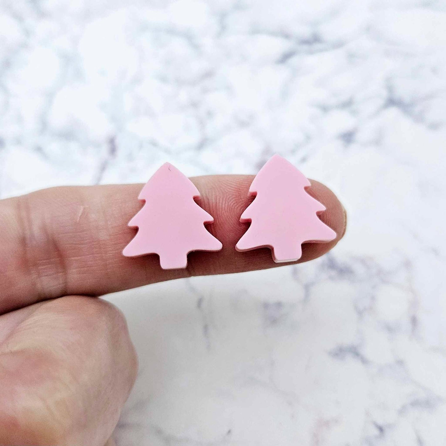 One pair of 16mm Pastel Pink acrylic Christmas tree stud earring blanks shown on a finger for size reference.
