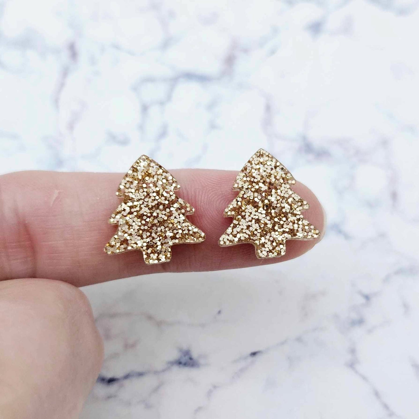 One pair of rose gold glitter acrylic 16mm Christmas tree stud blanks, shown on a finger for size reference.
