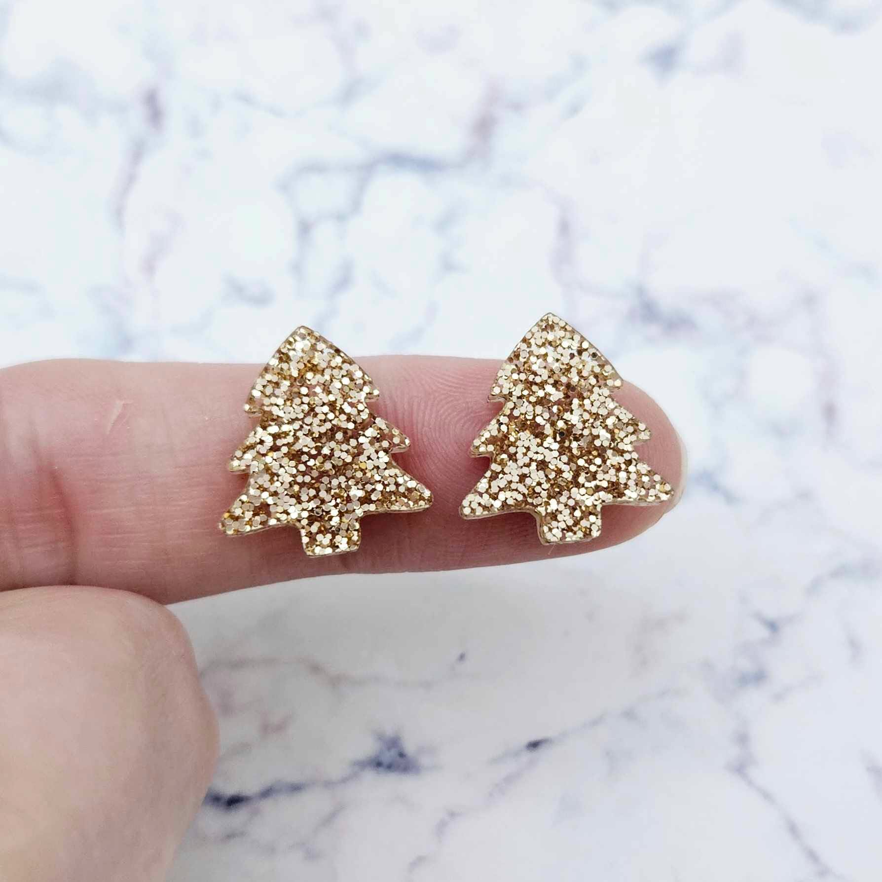 One pair of rose gold glitter acrylic 16mm Christmas tree stud blanks, shown on a finger for size reference.