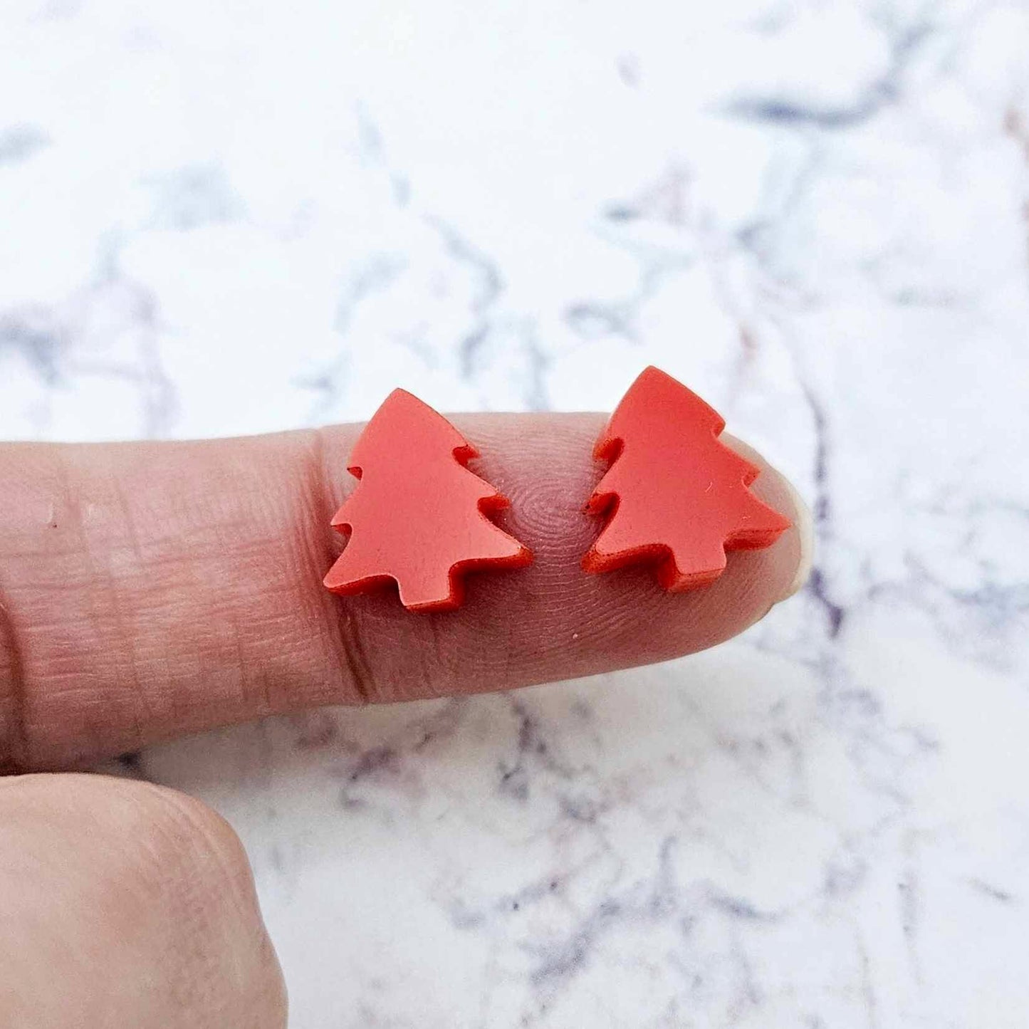 One pair of 12mm solid red acrylic Christmas tree stud earring blanks shown on a finger for size reference.