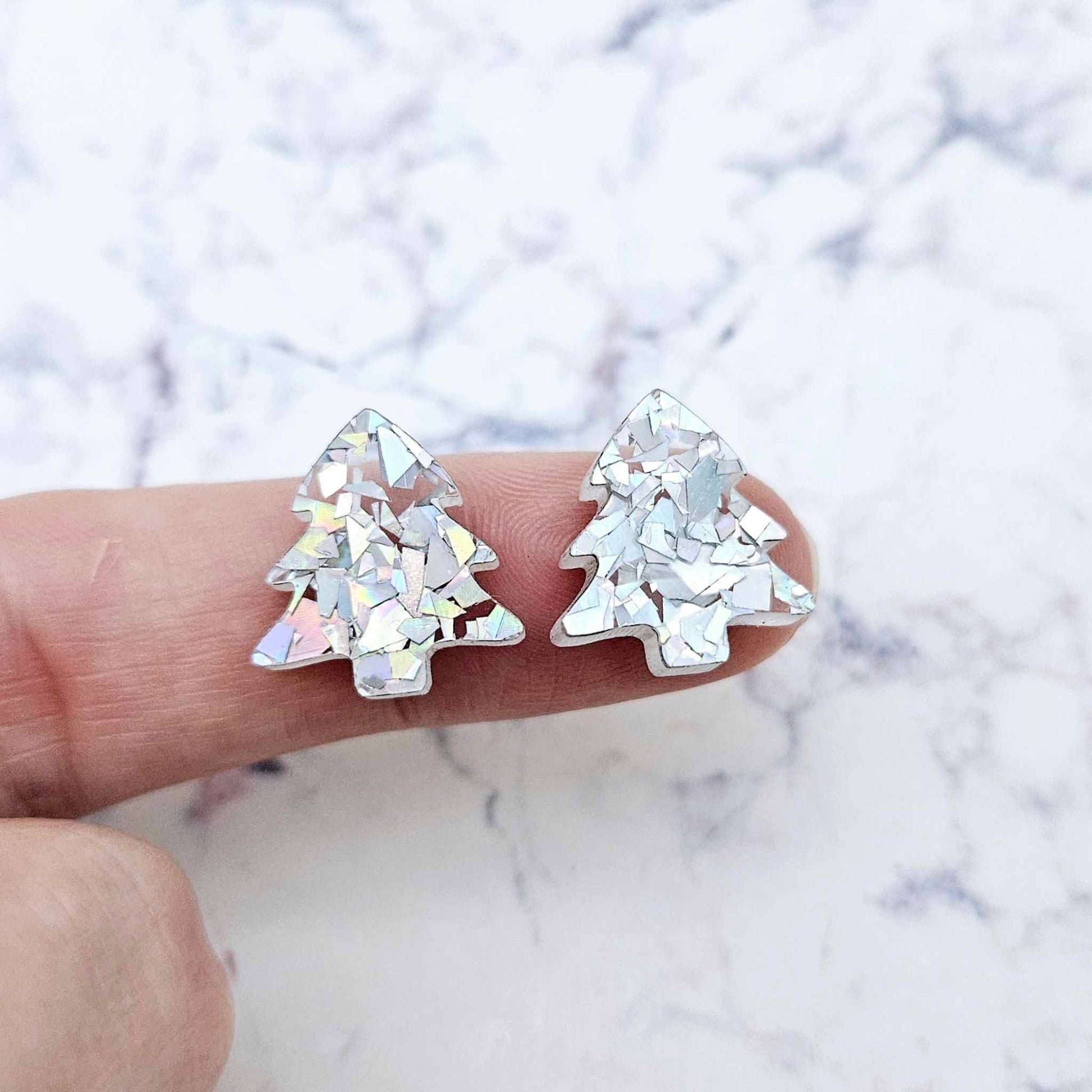 One pair of 16mm holographic silver glitter acrylic Christmas tree stud earring blanks – shown on a finger for size reference.