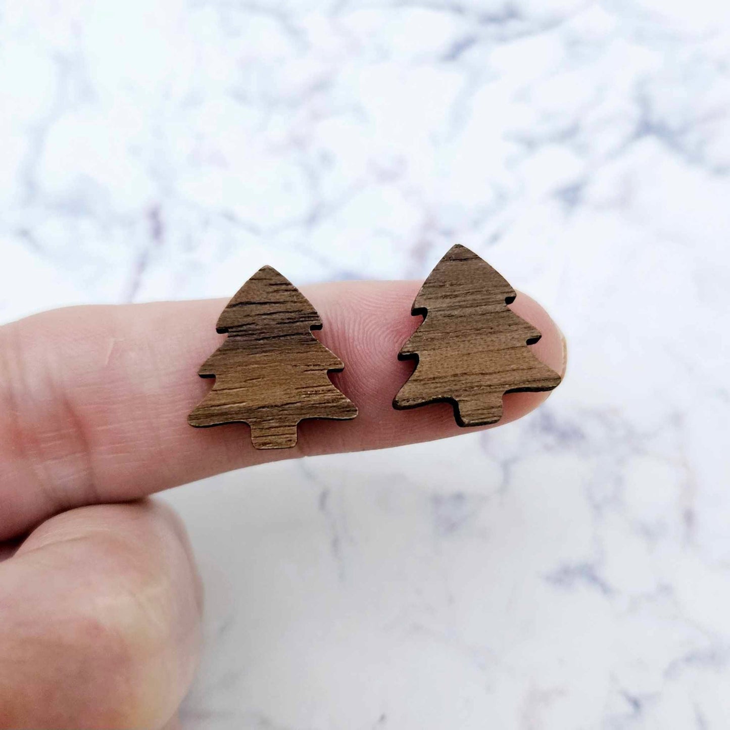 One pair of 16mm Walnut Veneer acrylic Christmas tree stud earring blanks shown on a finger for size reference.