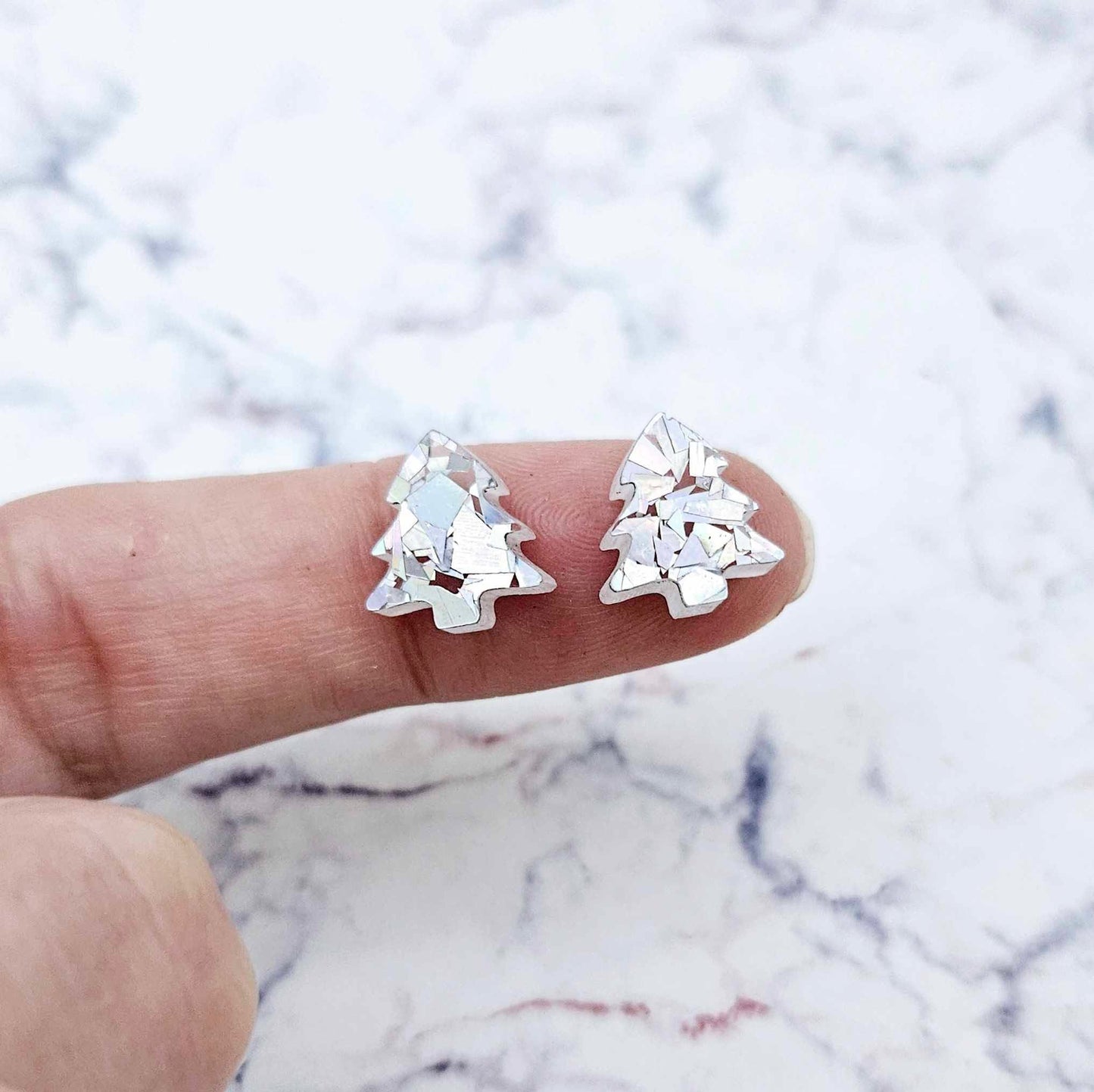 One pair of 12mm chunky holographic silver glitter acrylic Christmas tree stud earring blanks shown on a finger for size reference.