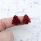 One pair of red glitter acrylic 16mm Christmas tree stud blanks, shown on a finger for size reference.