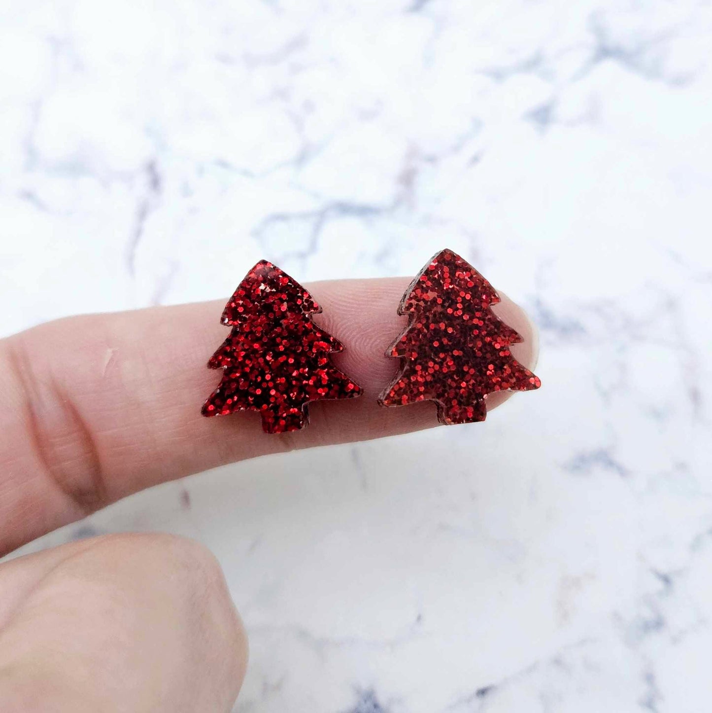 One pair of red glitter acrylic 16mm Christmas tree stud blanks, shown on a finger for size reference.
