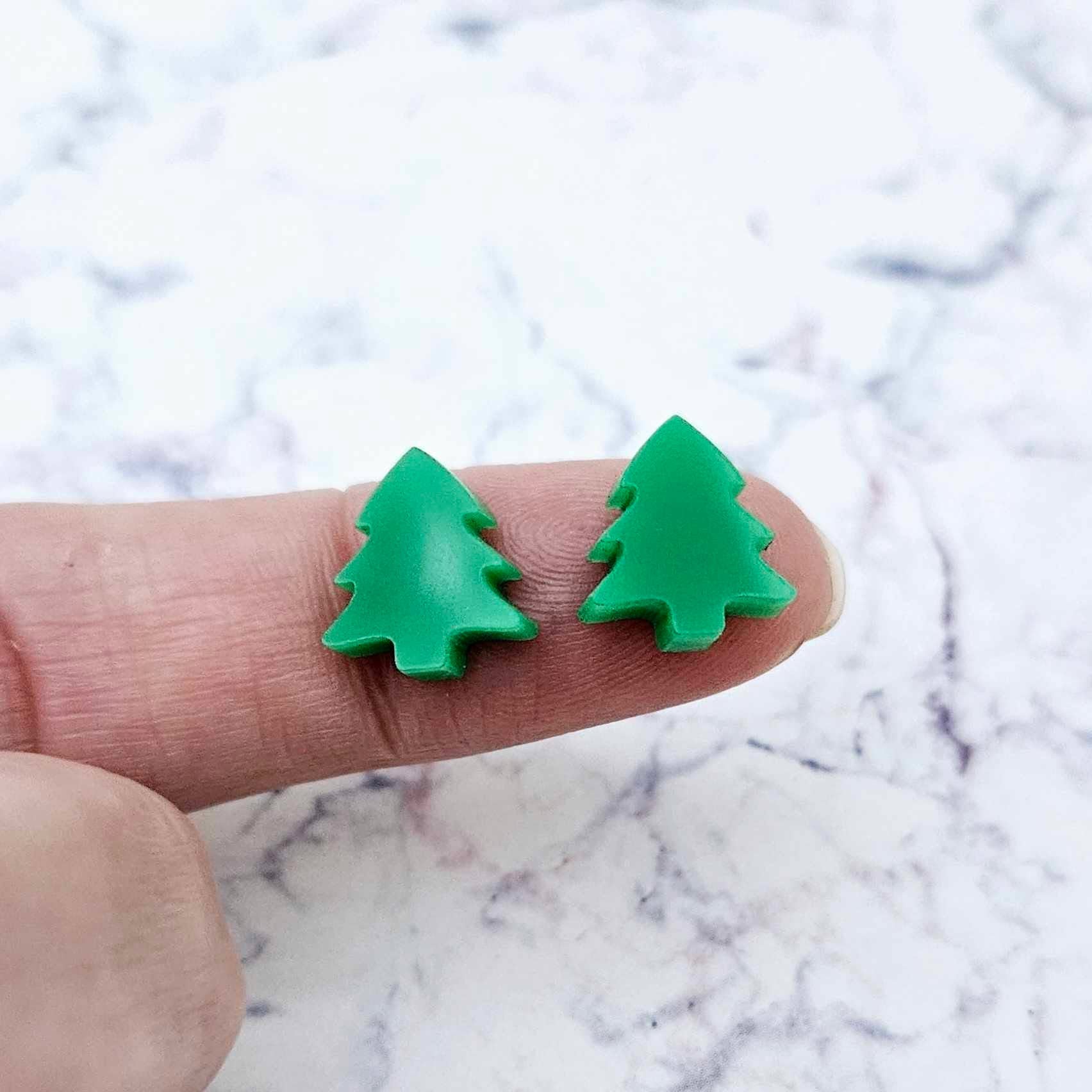 One pair of 12mm solid green acrylic Christmas tree stud earring blanks shown on a finger for size reference.