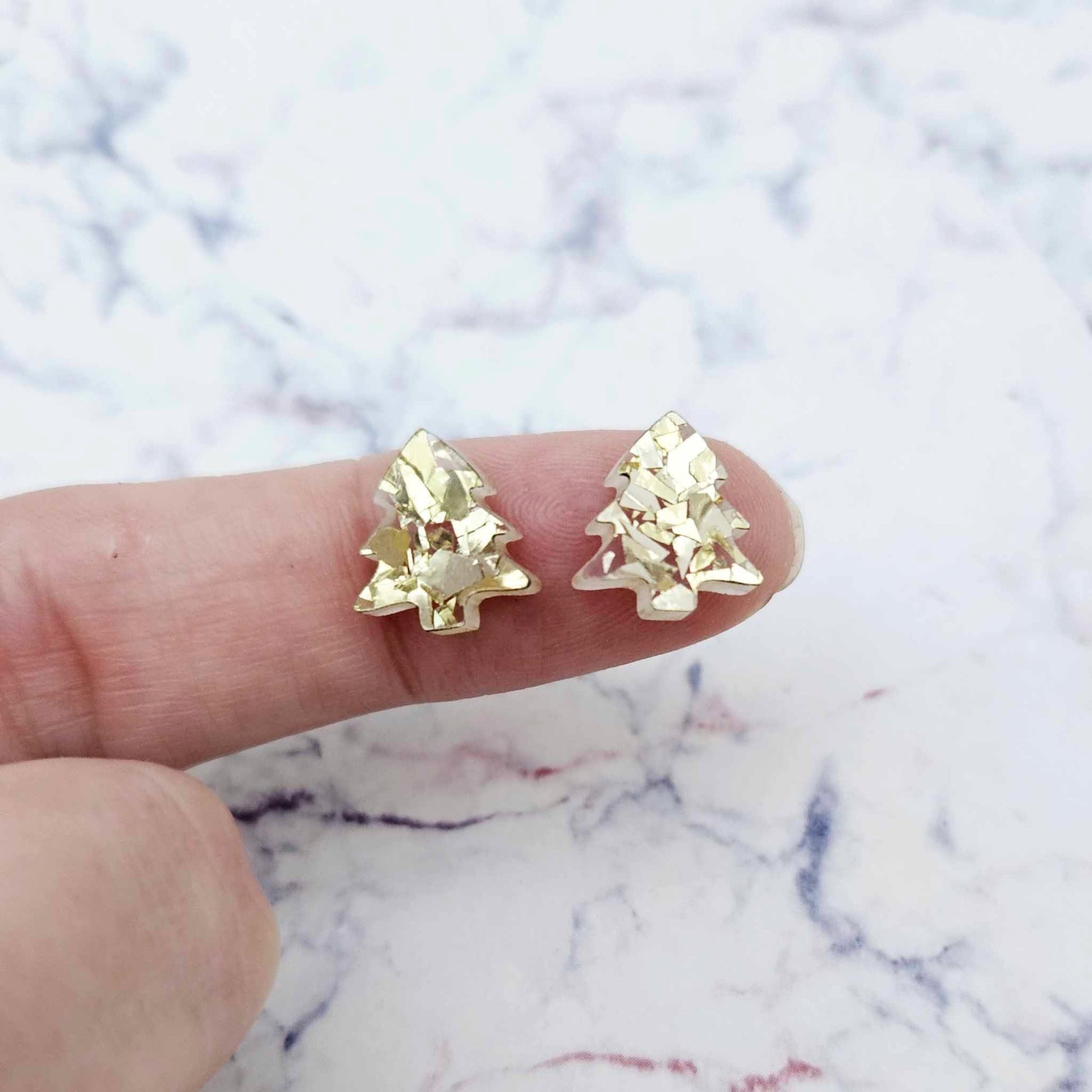 One pair of 12mm chunky gold glitter acrylic Christmas tree stud earring blanks shown on a finger for size reference.