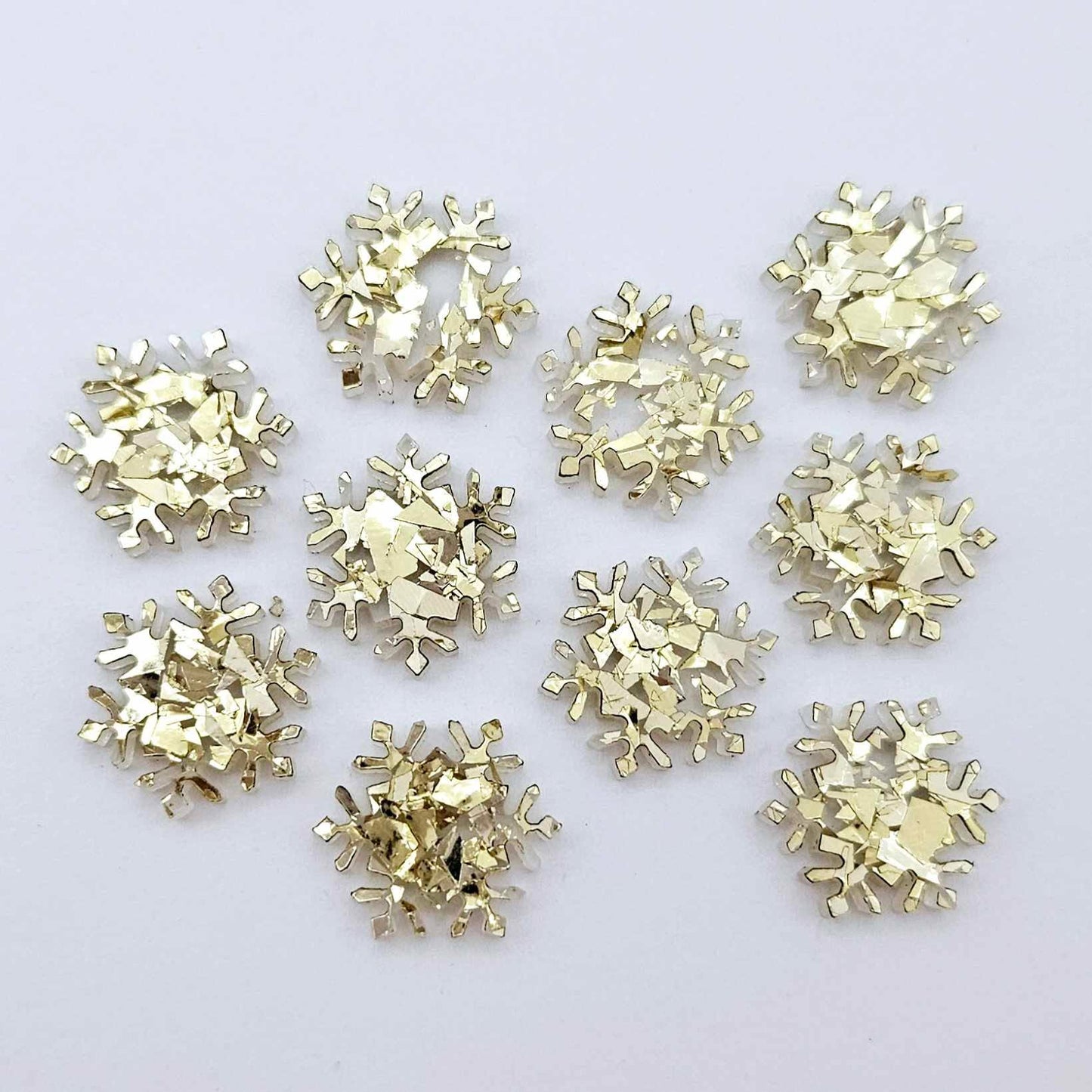 Five pairs of 16mm chunky gold glitter acrylic snowflake stud earring blanks laying flat.