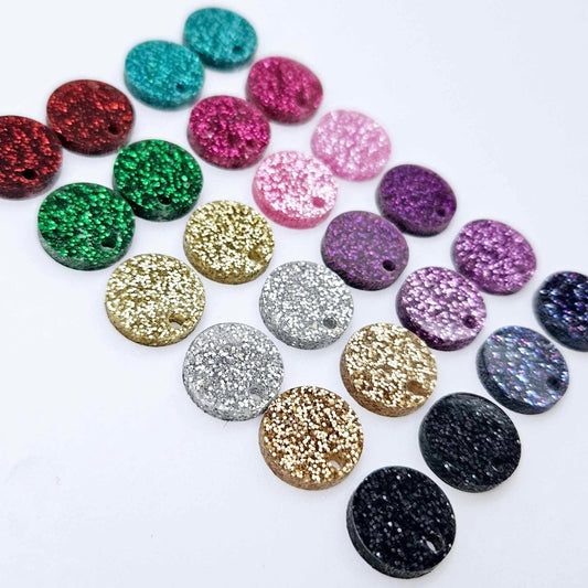 One pair of each 14mm fine glitter acrylic earring topper in 12 colours laying flat, including red, green, gold, silver, rose gold, black, teal, pink, purple and holographic glitters.