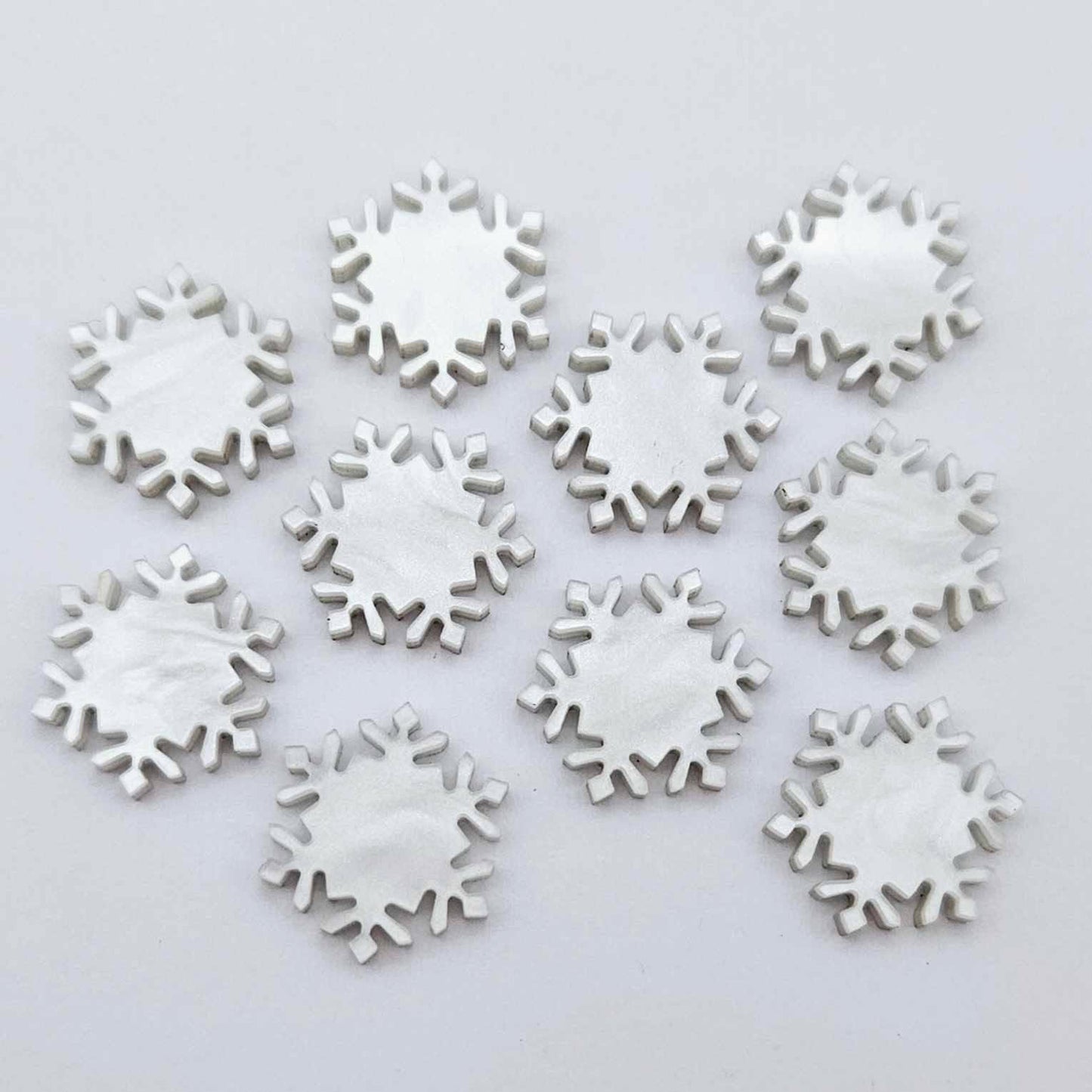 Five pairs of 16mm white marble acrylic snowflake stud earring blanks laying flat.