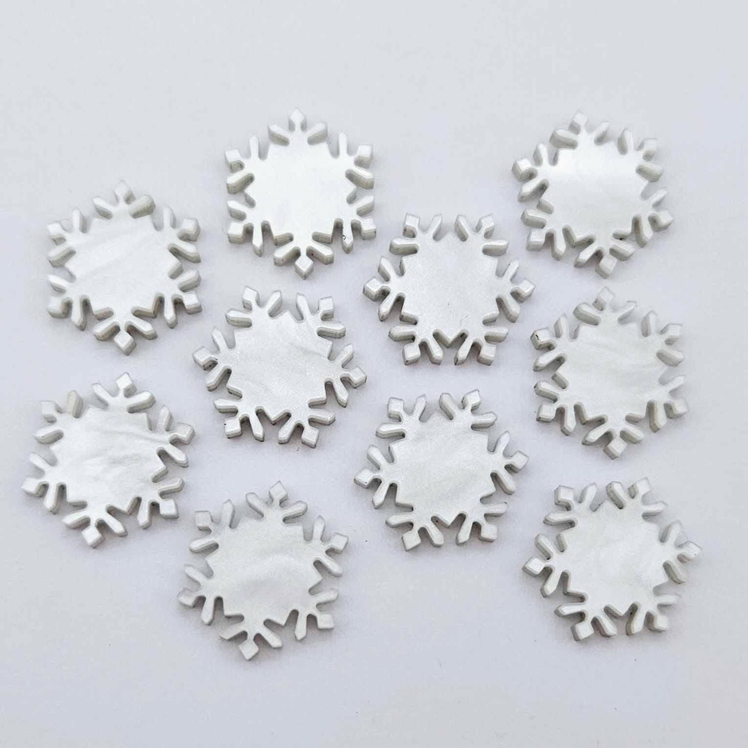 Five pairs of 16mm white marble acrylic snowflake stud earring blanks laying flat.