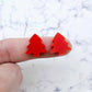 One pair of 16mm Solid Red acrylic Christmas tree stud earring blanks shown on a finger for size reference.