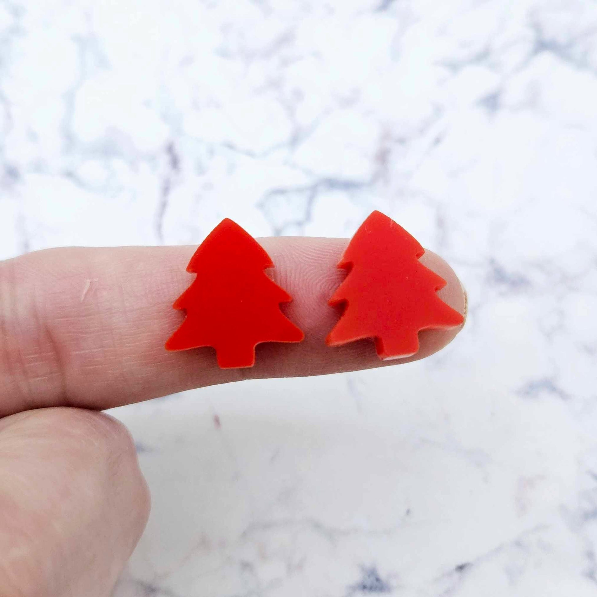 One pair of 16mm Solid Red acrylic Christmas tree stud earring blanks shown on a finger for size reference.