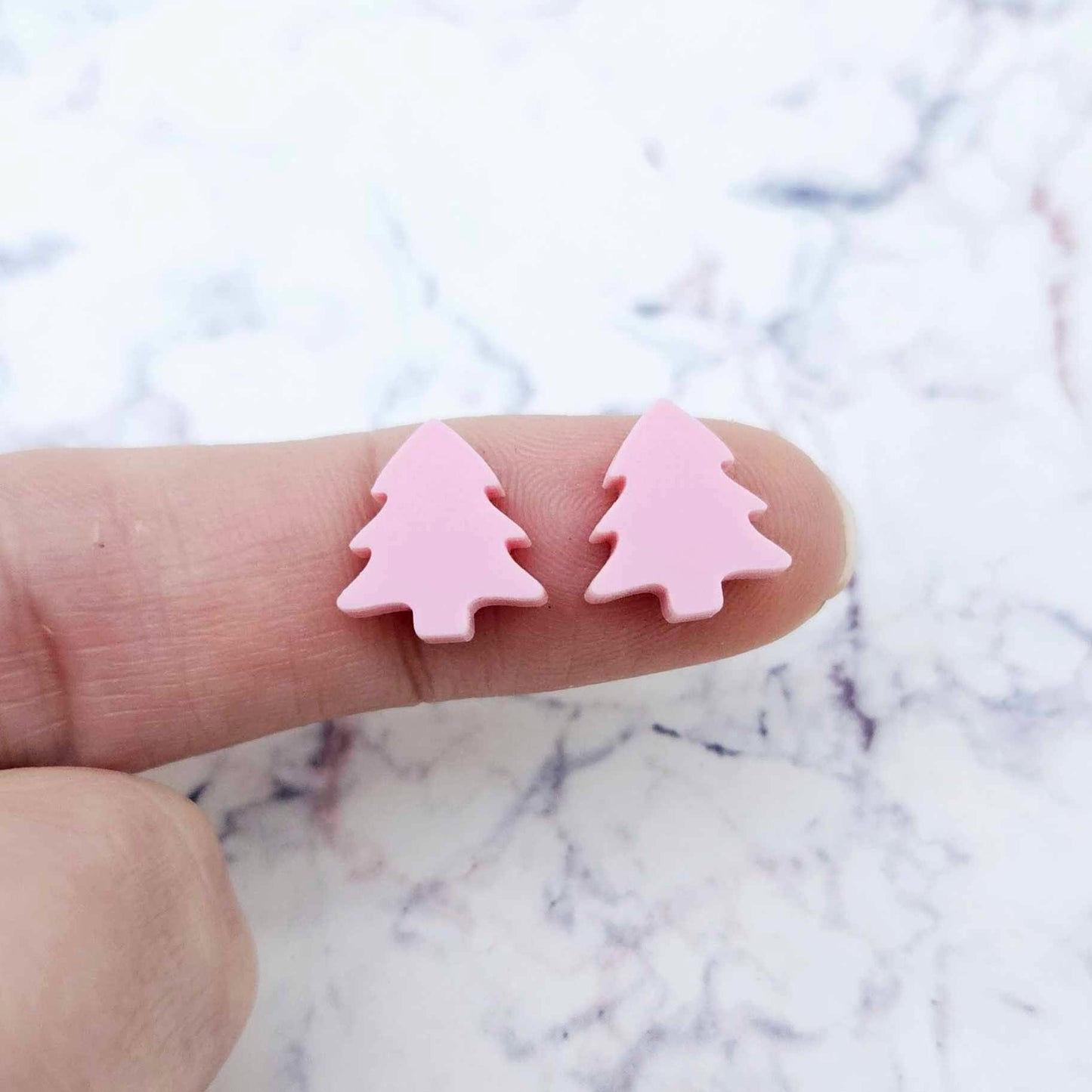 One pair of 12mm pastel pink acrylic Christmas tree stud earring blanks shown on a finger for size reference.